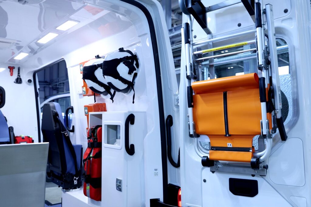 Folded ambulance stair chair mounted on the rear door, with two white rescue helmets hanging on the interior wall