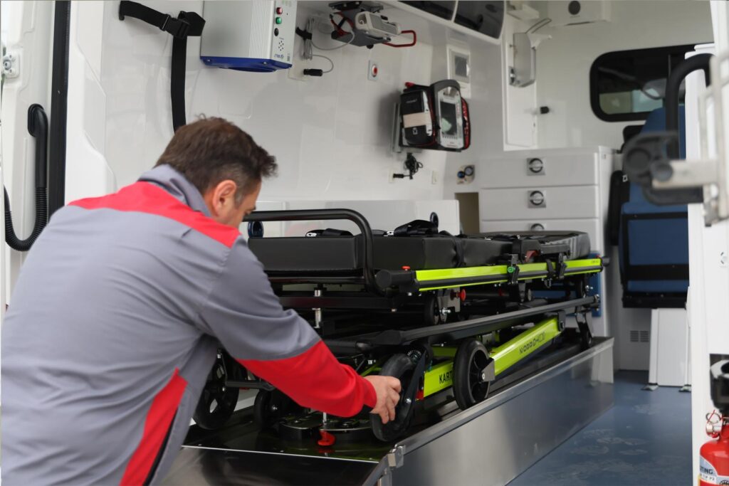 Paramedic loading a medical stretcher into the back of a modern ambulance.