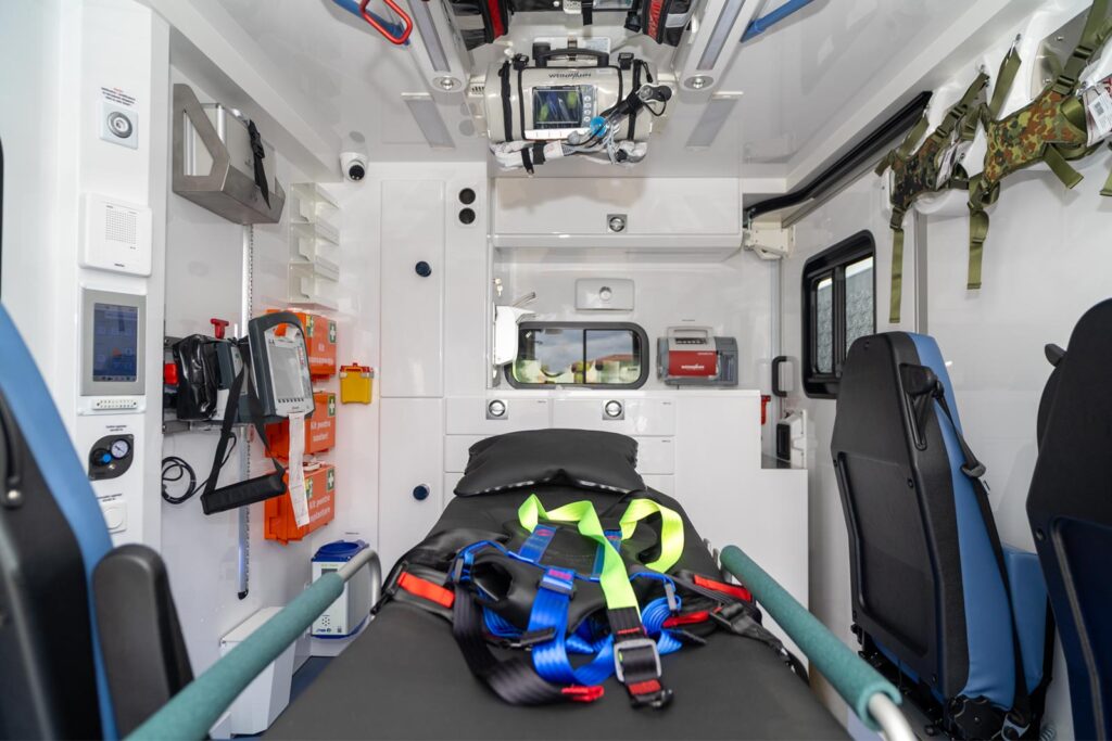 Interior of an ambulance medical cabin featuring a central patient stretcher surrounded by medical equipment.