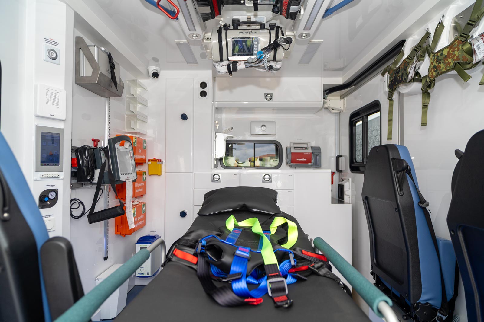 Interior of an ambulance medical cabin featuring a central patient stretcher surrounded by medical equipment.