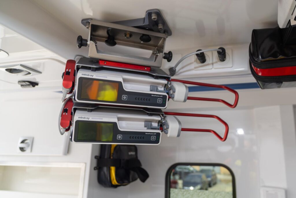 Close-up of two smart infusion syringe pumps stacked on a ceiling mount inside a modern emergency ambulance.